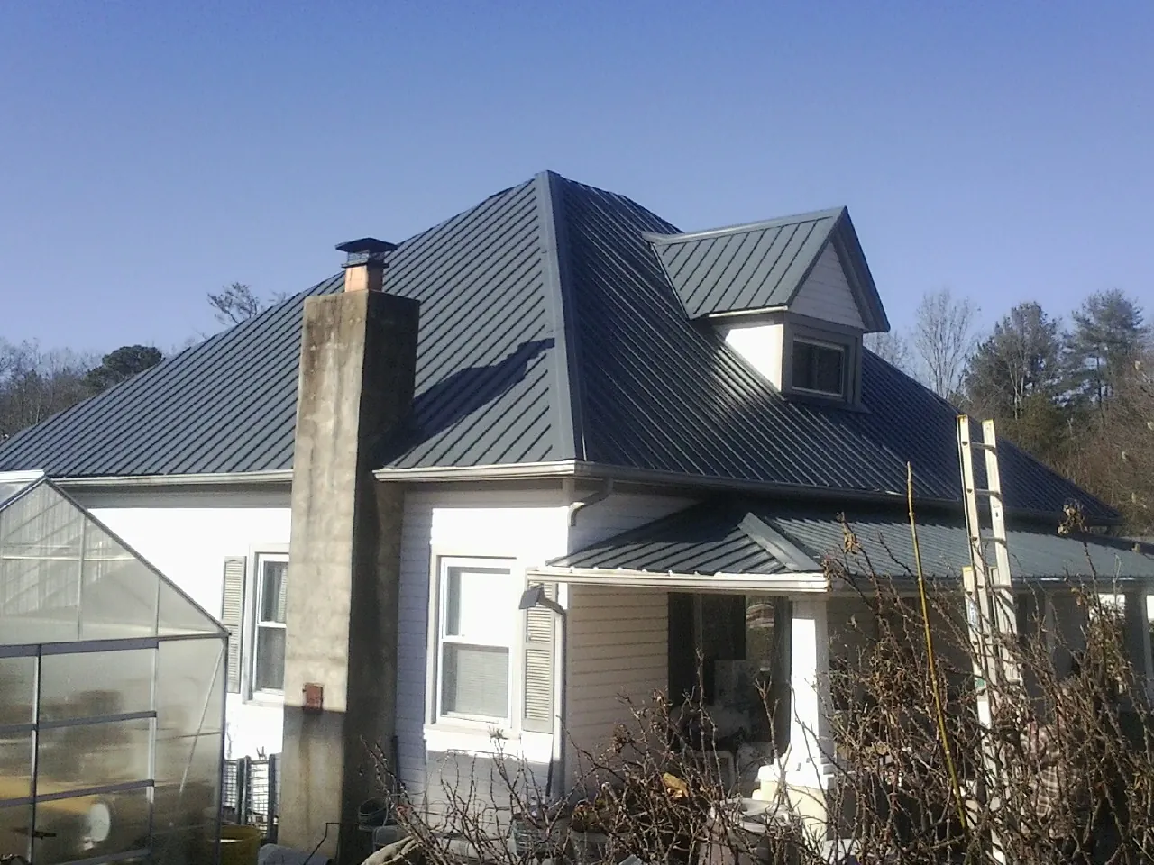 Dark blue standing seam metal roof on a white farmhouse with dormer — Slate & Tile Roof Repair by Roofing Brothers in Slater