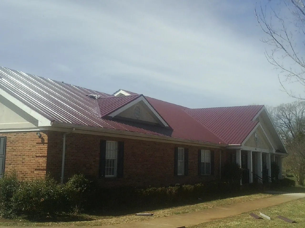 Red metal roof with gabled entries on a long brick building, from a Hail Damage Roof Repair job in Slater
