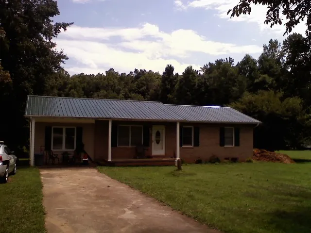 Dark green metal roof on a brick ranch with a covered porch in Slater