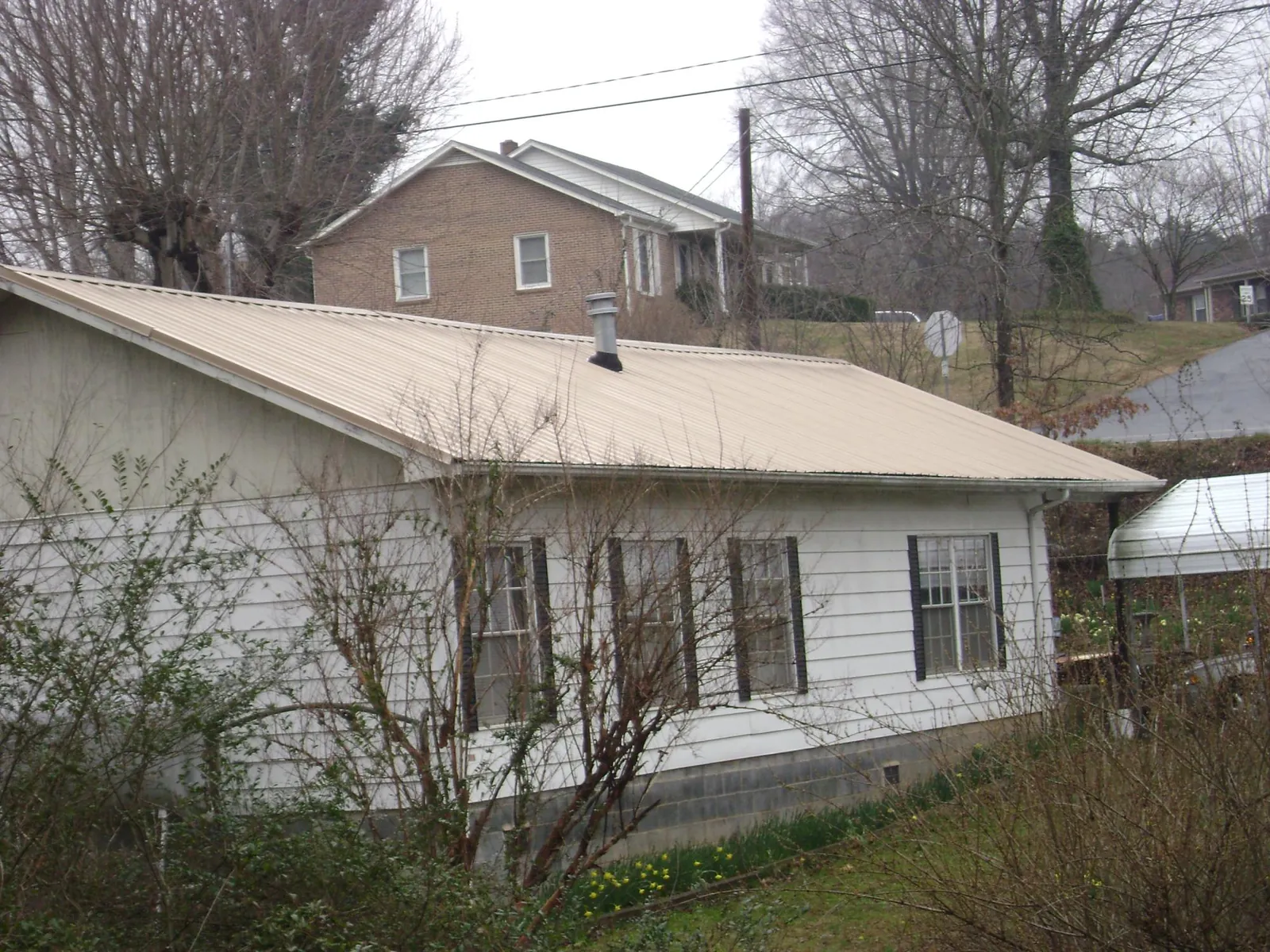 Tan metal roof on a white sided house set into a hillside — Commercial Roofing by Roofing Brothers in Slater